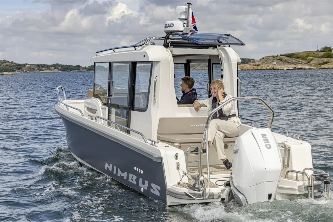 A Nimbus boat navigates through water, featuring two people onboard, one seated and the other relaxing, with visible motor details.